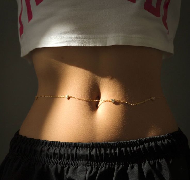 Person wearing a gold waist chain with a dark background