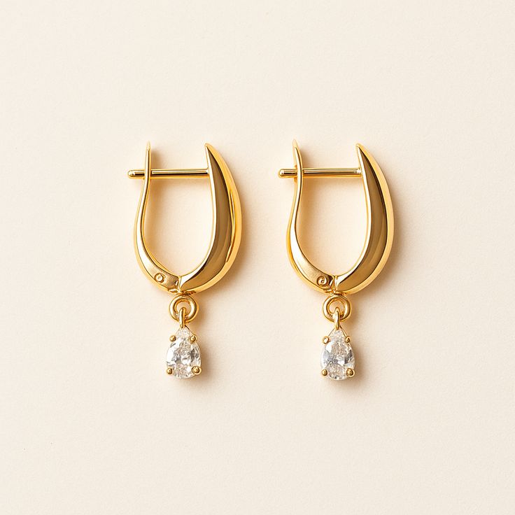 Gold hoop earrings with diamond drops on a beige background