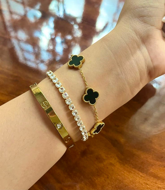 Gold bracelets with clover and diamond designs on a wrist against a wooden background