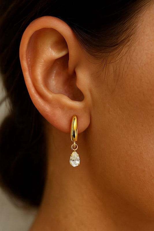 Gold hoop earring with a clear gemstone worn by a person.