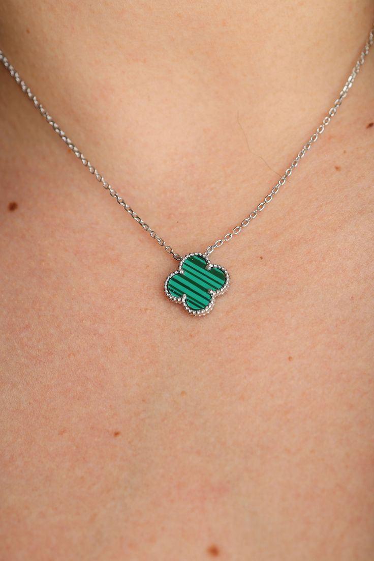 Green clover-shaped pendant on a silver chain against a skin background