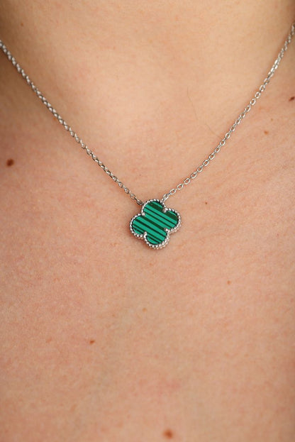 Green clover-shaped pendant on a silver chain against a skin background