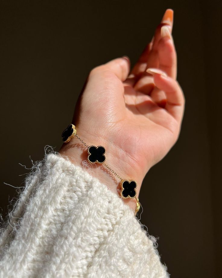Hand wearing a bracelet with black clover-shaped charms against a dark background