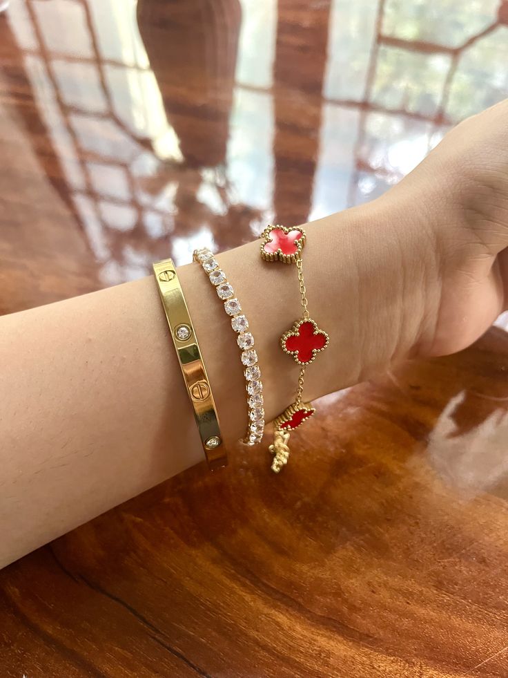Close-up of a wrist wearing multiple bracelets with red and gold clover love band 