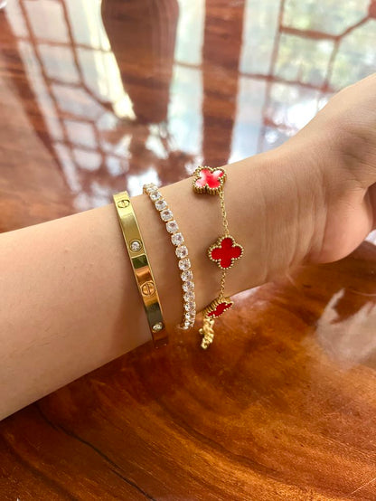 Close-up of a wrist wearing multiple bracelets with red and gold clover love band 