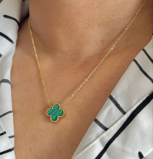 Gold necklace with a green clover pendant worn by a person against a white and black striped background
