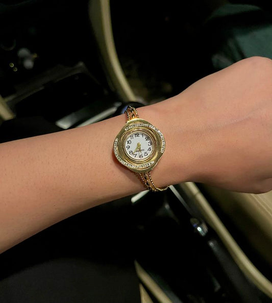 Gold wristwatch with a white face on a wrist, blurred background